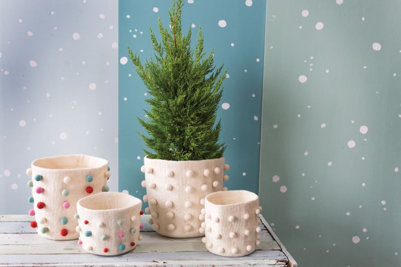 Evolution Home Decors FELT POM POT COVER with cute pom pom balls for a stylish addition to your home decor. Shown styled with christmas trees and shows other color pom pot covers.